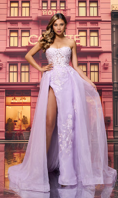 A woman poses in front of a pink building, wearing the Long Prom Dress: Colette CL8660—a strapless ball gown with a sheer lace bodice, embroidered A-line skirt, floral details, and a high slit.