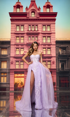 A woman poses confidently in front of a pink hotel wearing the Colette CL8660 Long Prom Dress—a lilac strapless ball gown featuring a sheer lace bodice and high slit.