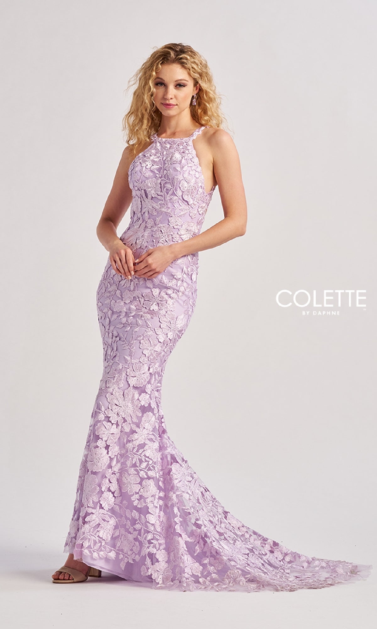 A woman stands gracefully in the Colette CL8665 long prom dress—a stunning purple mermaid gown with a high square neckline for elegance and an open back adding a modern twist.