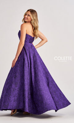A woman poses in the floor-length purple Colette CL8675 prom dress with an A-line skirt, textured pattern, and pockets, standing against a plain light background.