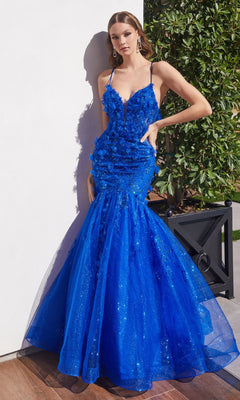A woman poses outdoors in the Lace-Up Long Mermaid Shimmer Prom Dress CM328, a vibrant blue, floor-length gown with floral appliqués, thin straps, and a fitted bodice.