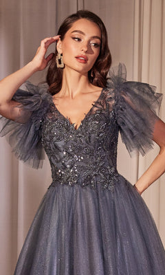 A woman stands indoors against a neutral curtain, wearing the Ladivine CM359 Flutter-Sleeve Blue Prom Ball Gown with sheer flutter sleeves, intricate beadwork, and a sequin-lace bodice.