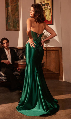 A woman in an emerald Cut-Out Strapless Long Prom Dress (Ladivine CM378) faces away, while a man in a dark suit sits at a small table in a dim room decorated with vintage wall art.