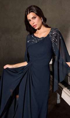 A woman poses indoors near a white piano, elegantly holding her dark blue Ladivine CR884 long formal chiffon dress with embellished cape sleeves.