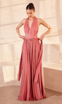 A woman indoors adjusts the sash of the Amoris CV01 Multi-Wrap Long A-Line Prom Dress, a sleeveless rose-pink gown with a halter neckline.