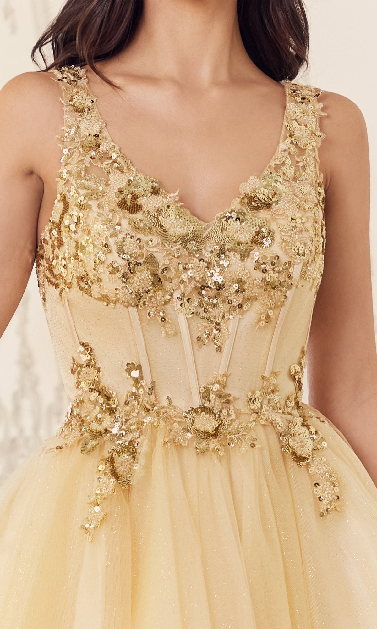A woman wears the Sequin-Corset Short A-Line Homecoming Dress CY019, a sleeveless light yellow gown with gold floral embroidery and sequins, featuring a fitted sheer bodice styled like an affordable cocktail dress.