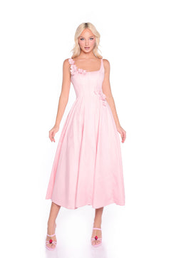 A woman wearing the Blush Pink A-Line Midi Casual Dress: Camellia with matching pink heels stands against a white background. The dress features 3D flowers on the bodice and an elegant sleeveless design.