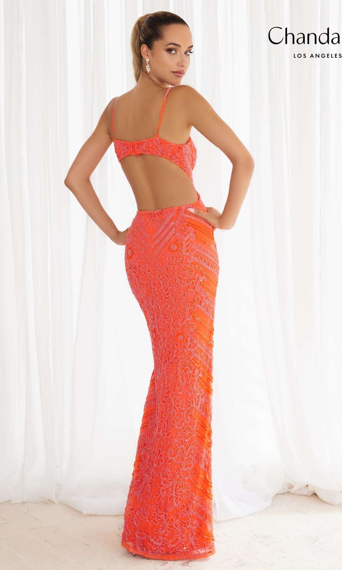 A woman stands with her back to the camera wearing Chandalier's Long Prom Dress 30129—a bright orange beaded formal gown with thin straps and an open back.