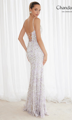 A woman stands before sheer white curtains in the Long Prom Dress 30157 by Chandalier, a light lavender, floor-length fitted formal gown with floral embroidery and a lace-up back.