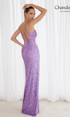 A woman stands in front of white curtains wearing the Long Prom Dress 30158 by Chandalier—a floor-length lavender sequin gown with spaghetti straps and an open back lace-up detail.