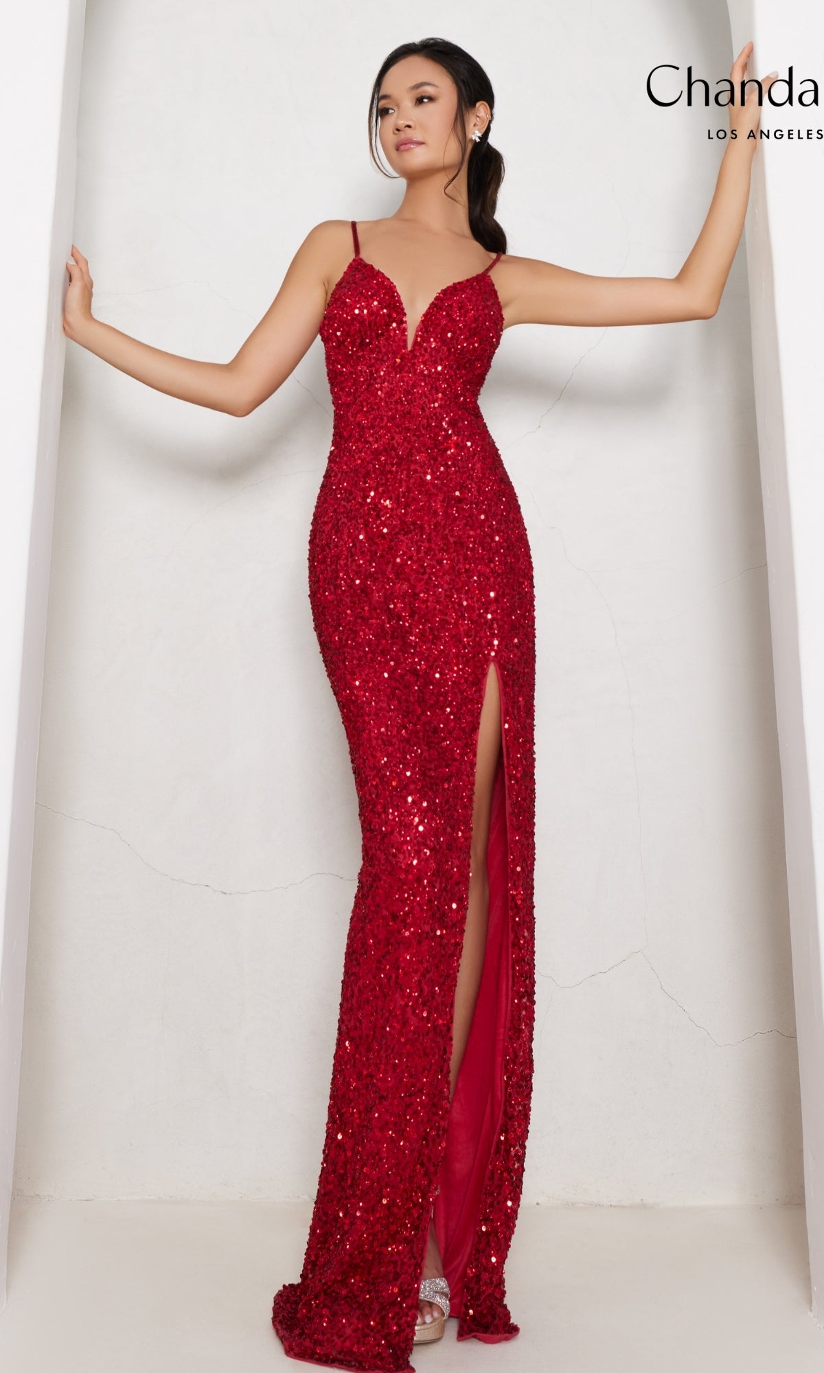A woman poses in the Long Prom Dress 30161 by Chandalier—a red sequin formal gown featuring spaghetti straps and a thigh-high side slit—against a white background.