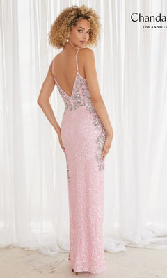 A woman with curly blonde hair wears the Long Formal Dress 30171 by Chandalier, a light pink sleeveless sequin gown with silver embellishments and a v-neckline, standing before sheer white curtains.