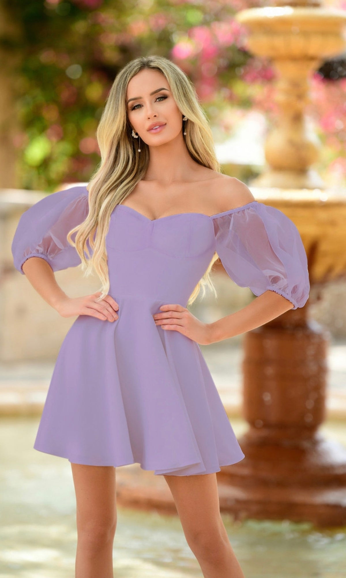 Woman wearing the Chloe Short White Puff-Sleeve Party Dress, standing outdoors in front of a blurred fountain and greenery.