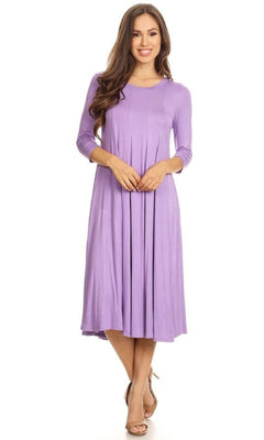 A woman stands against a white background, smiling with hands clasped in front, wearing a lavender Knee-Length Casual Party Dress with long sleeves and nude heels.