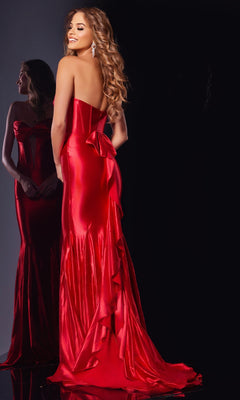A woman stands and smiles in front of a mirror wearing the Jovani D5119 long red prom dress, featuring a strapless corset bodice, floor-length satin skirt, and a bow detail on the back.
