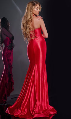 A woman wearing the Jovani D5306 Long Prom Dress—a shiny, form-fitting red gown with a corset bodice and lace-up back—stands with her back to the camera as her reflection is seen in a mirror to the left.