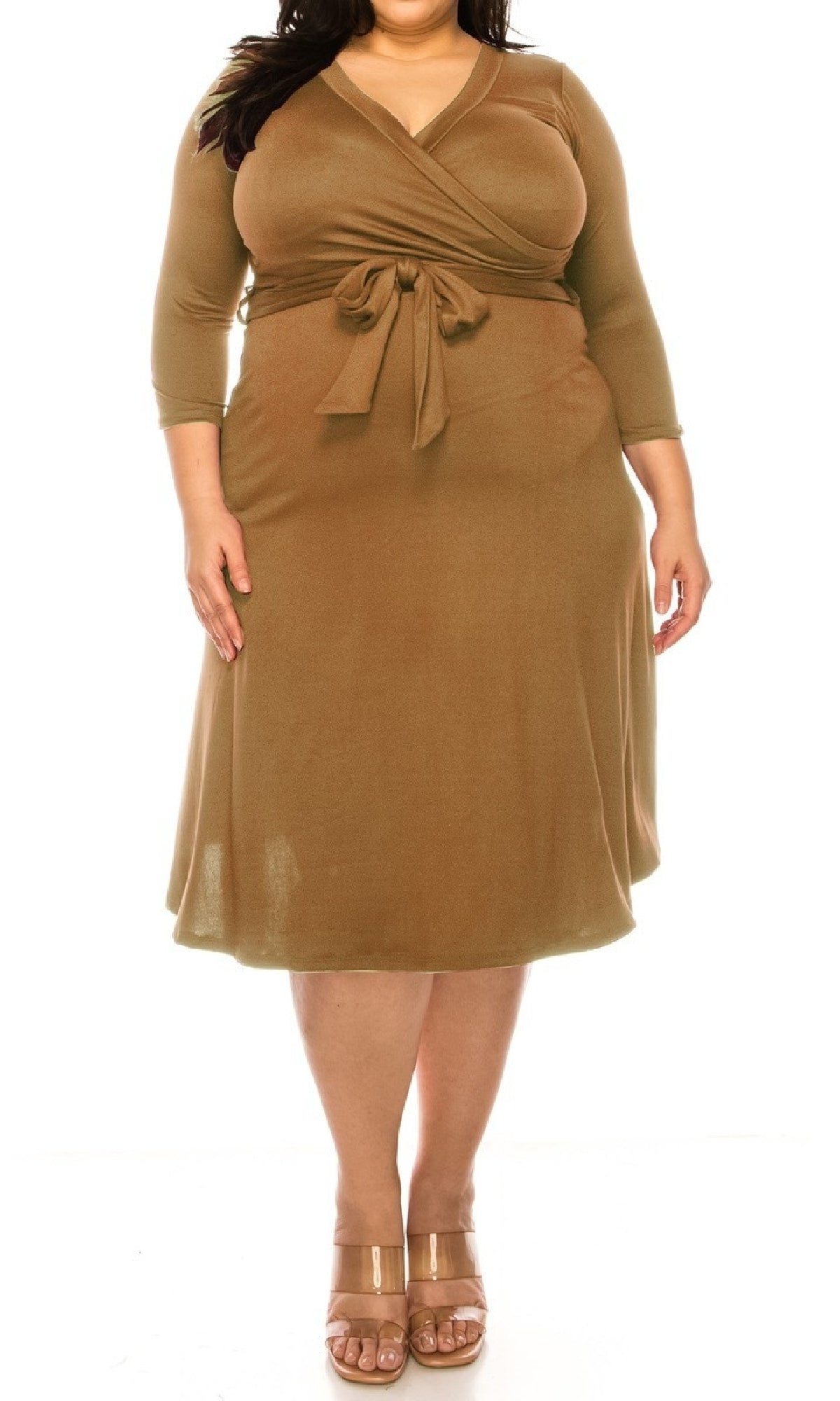 A woman models the Faux-Wrap Plus-Size Casual Dress with Sleeves in brown, featuring a knee-length cut, long sleeves, and a waist tie. She pairs it with beige heeled sandals and stands against a white background.