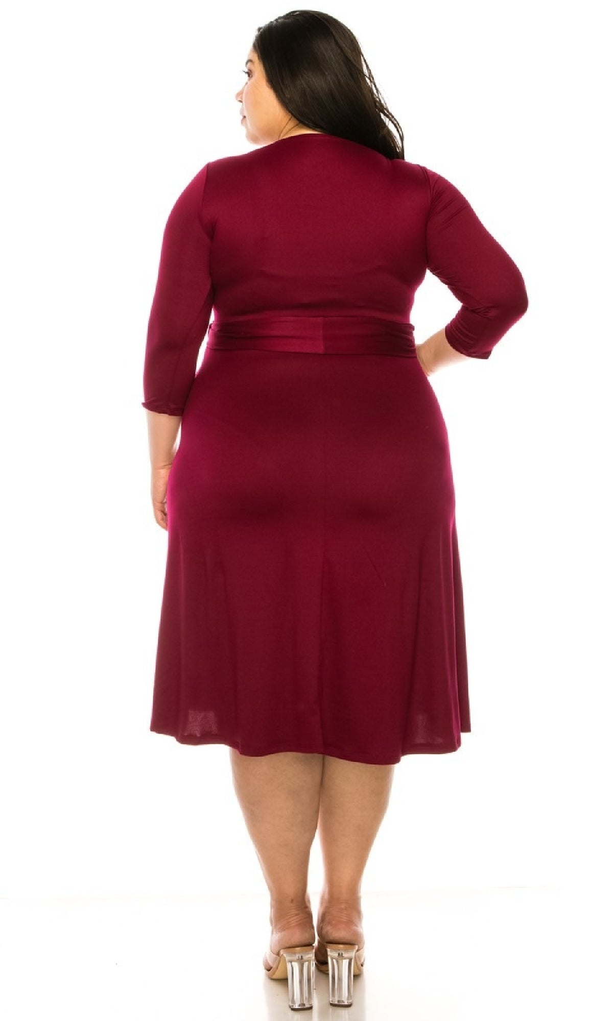 A woman stands facing away in a knee-length Faux-Wrap Plus-Size Casual Dress with sleeves, paired with clear-heeled sandals, set against a white background.