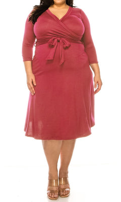 A woman models the Faux-Wrap Plus-Size Casual Dress with Sleeves in magenta, featuring long sleeves and a waist tie, paired with tan heeled sandals against a white background.