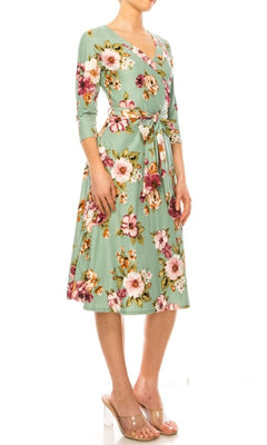 A woman wearing the Sage Green Floral Print Faux-Wrap Casual Dress with three-quarter sleeves and a waist tie, styled with clear heeled sandals.