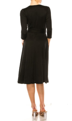 A woman faces away, wearing the Faux-Wrap Casual Short Dress with Sleeves—knee-length, black, v-neckline, three-quarter sleeves—styled with clear-heeled sandals against a white background.