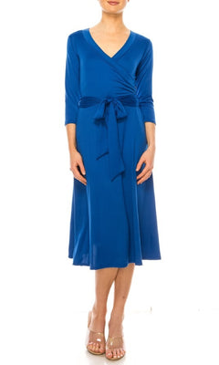 A woman models the Faux-Wrap Casual Short Dress with Sleeves—a knee-length, blue dress featuring long sleeves, a waist tie, and v-neckline—styled with beige open-toe heels against a white background.