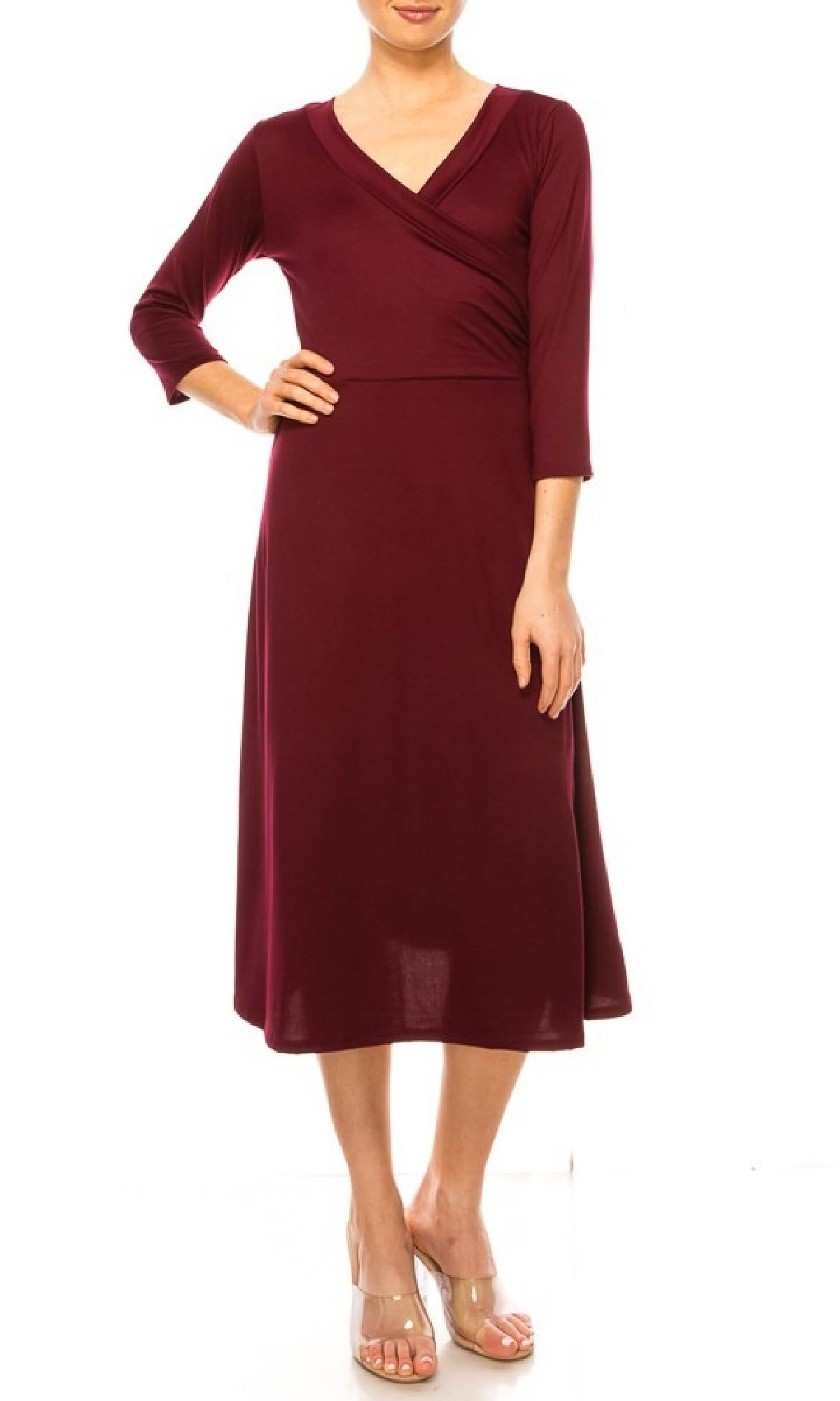A woman stands against a white background wearing the Faux-Wrap Casual Short Dress with Sleeves in burgundy, featuring a knee-length cut, long sleeves, and V-neckline, paired with clear wedge sandals.
