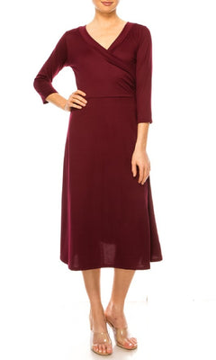 A woman stands against a white background wearing the Faux-Wrap Casual Short Dress with Sleeves in burgundy, featuring a knee-length cut, long sleeves, and V-neckline, paired with clear wedge sandals.