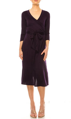 A woman models the Faux-Wrap Casual Short Dress with Sleeves in dark purple, featuring a v-neckline, three-quarter sleeves, and waist tie, paired with nude heels against a white background.