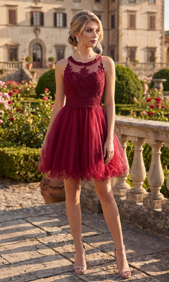 A woman wearing the Chicas DM4002 Short Homecoming Dress in burgundy, featuring a sleeveless fit-and-flare silhouette with an embroidered bodice, stands on a stone patio in a garden surrounded by trimmed bushes, flowers, and a historic building in the background.