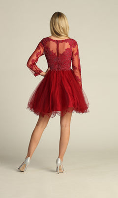A woman faces away, wearing the Beaded Long Sleeve Short Homecoming Dress DM4003 with a sheer, beaded bodice and long sleeves, paired with silver high heels against a plain background.