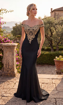 A woman in the Chicas DM4011 long formal dress, featuring an off-the-shoulder design with an intricately embroidered bodice and gold appliques in black, stands outdoors on a stone path surrounded by lush greenery and blooming flowers.