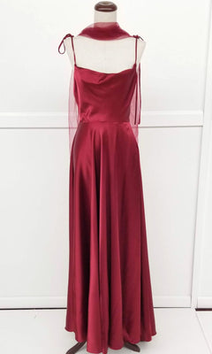 The Shoulder-Tie Long A-Line Prom Dress Chicas DM4018 is a sleeveless, floor-length burgundy satin gown with a cowl neckline and sheer shoulder ties, showcased on a dress form against a plain white background.