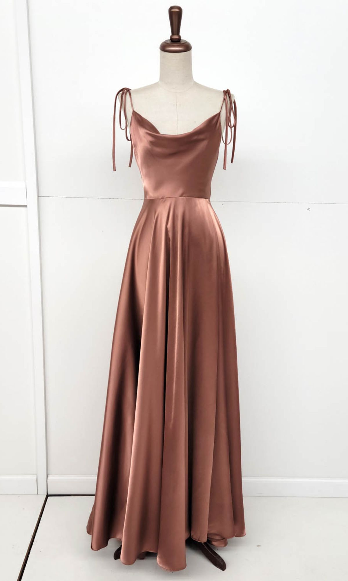 The Shoulder-Tie Long A-Line Prom Dress (Chicas DM4018), a floor-length copper satin gown with a cowl neckline and tied spaghetti straps, is displayed on a dress form against a white background.