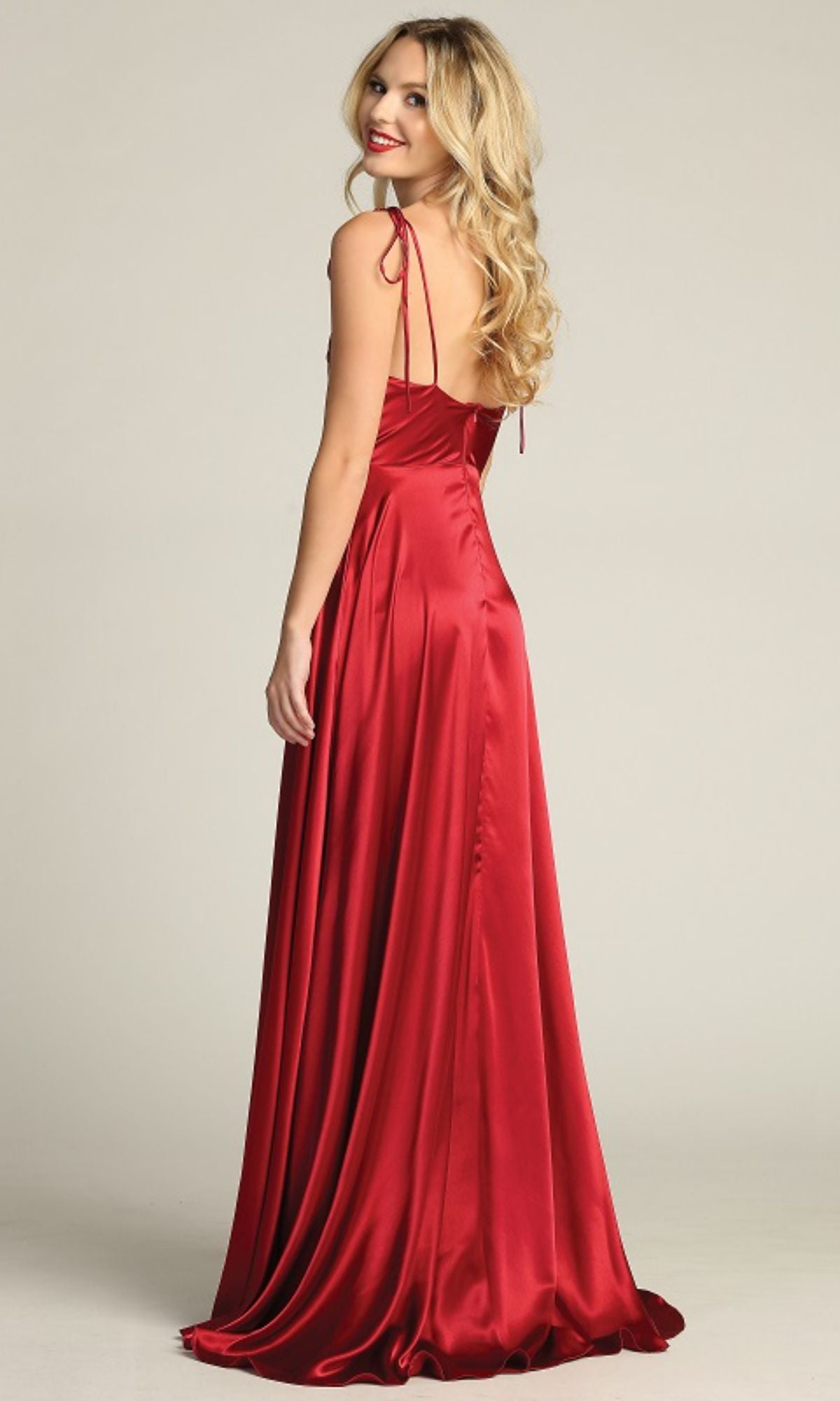 A woman with long blonde hair poses in the Chicas DM4018 Shoulder-Tie Long A-Line Prom Dress—a floor-length, sleeveless red evening gown—looking over her shoulder against a plain background.