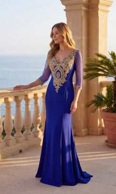 A woman in the Long Formal Dress: Chicas DM4020, featuring a royal/gold hue and v-neck embroidery, stands on a sunlit terrace overlooking the sea.