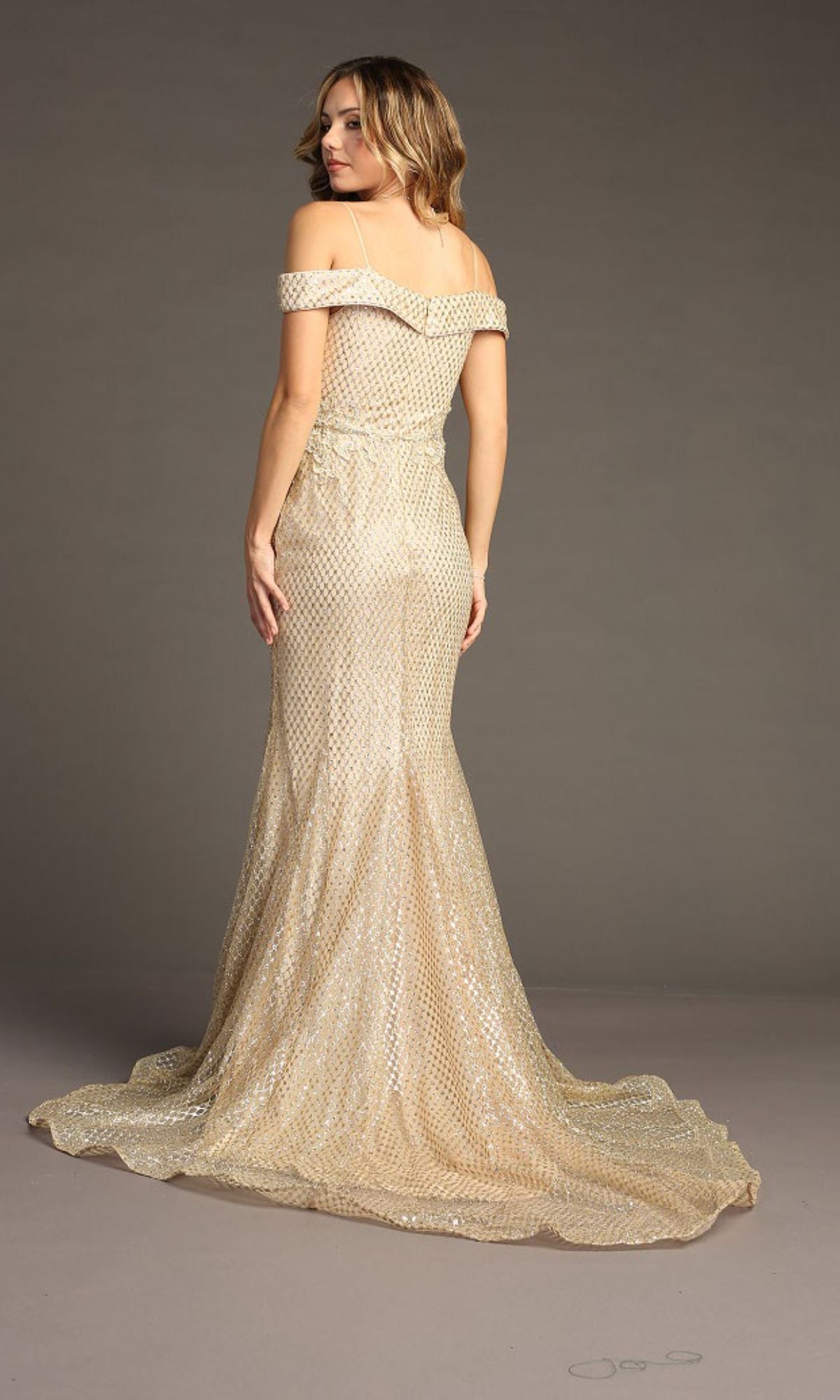 A woman in the Off-the-Shoulder Long Prom Dress: Chicas DM4024, styled with a subtle shimmer and mermaid silhouette, stands facing away against a plain background.