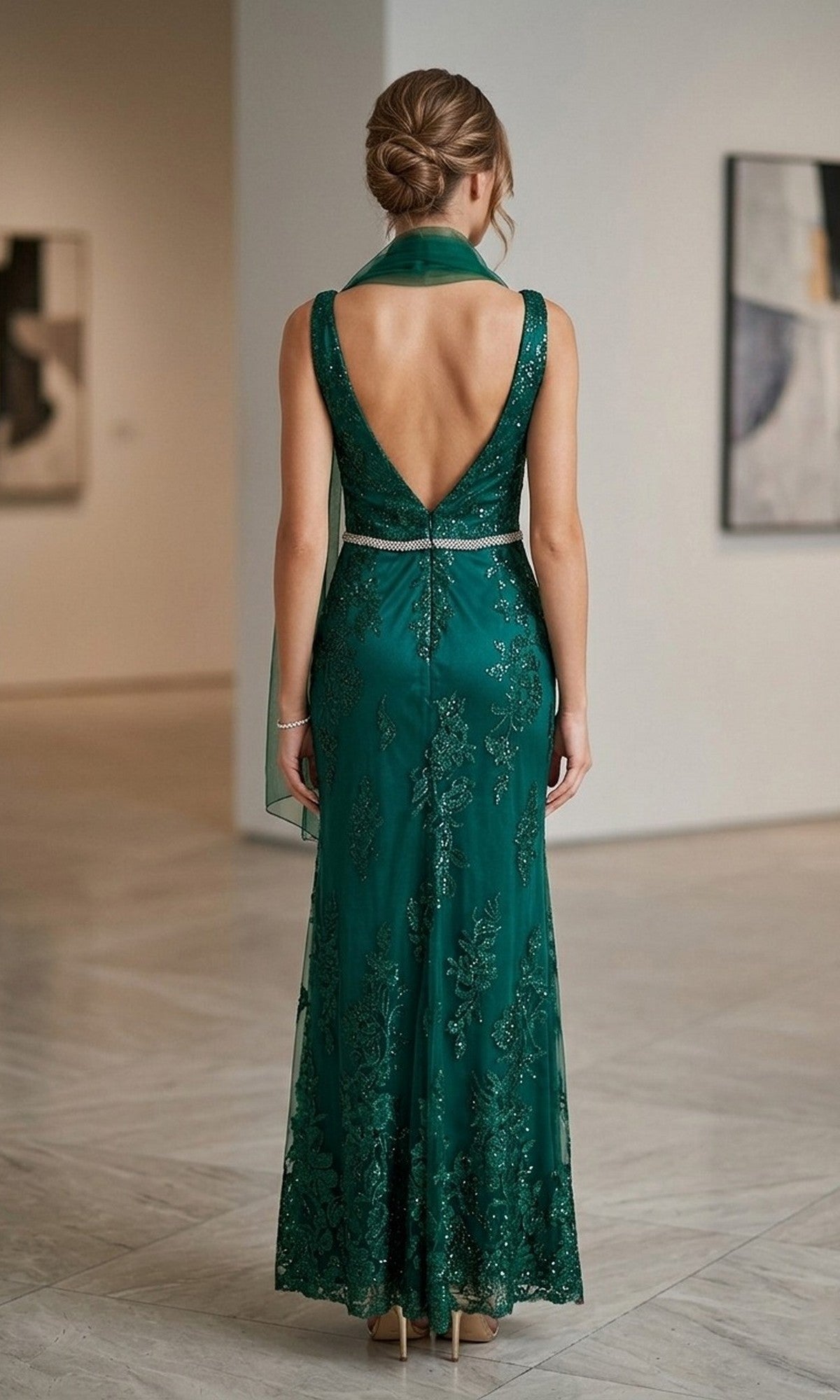 A woman stands indoors on a marble floor, facing away from the camera, wearing the Chicas DM4026 Long Formal Dress—an emerald green, floor-length, sleeveless gown with a deep V-back.