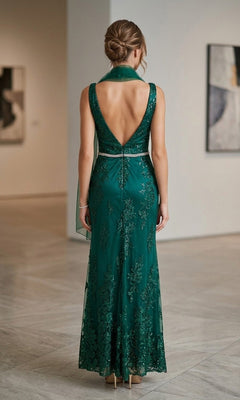 A woman stands indoors on a marble floor, facing away from the camera, wearing the Chicas DM4026 Long Formal Dress—an emerald green, floor-length, sleeveless gown with a deep V-back.