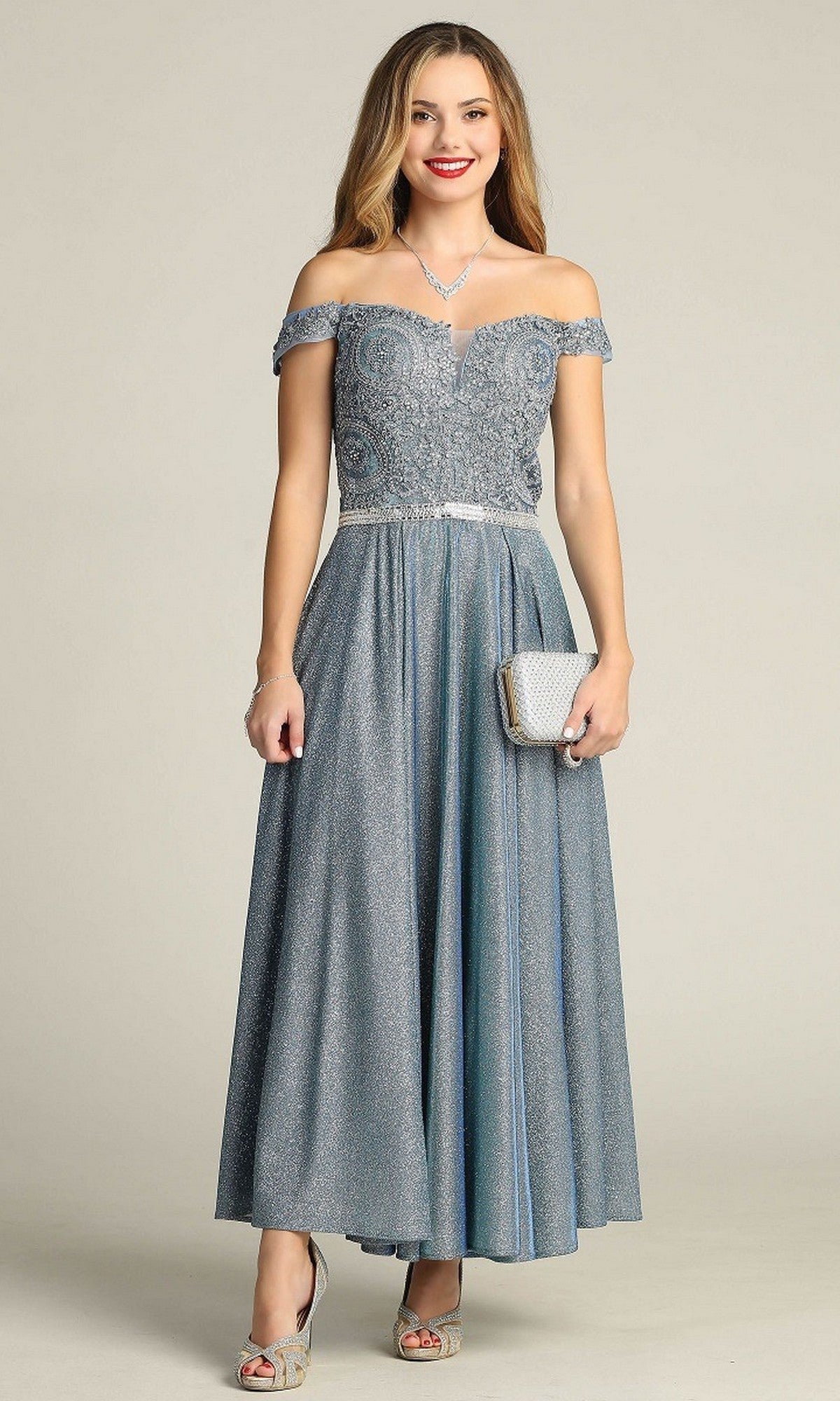A woman in a blue Tea-Length Formal Dress: Chicas DM4027 with an embroidered bodice, holding a silver clutch and accessorized with silver heels and jewelry, stands against a plain background.