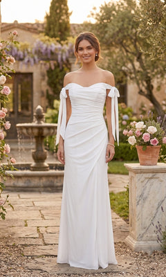 A woman in the Long Prom Dress: Chicas DM8010 in off white, featuring an off-the-shoulder design and a thigh-high slit, stands outdoors by a stone fountain and potted flowers, surrounded by greenery.