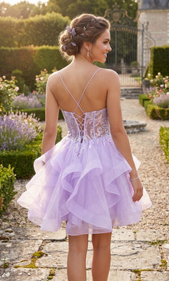 A young woman stands outdoors on a stone path surrounded by gardens, facing away from the camera, wearing the Short Homecoming Dress: Chicas DM8031—a lilac, ruffled, fit-and-flare dress with a lace-up back.