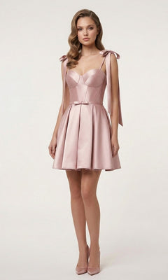 A woman stands against a plain background, wearing the Chicas DM8133 short homecoming dress in blush—a fit-and-flare satin style featuring a fitted corset bodice, flared skirt, and bow accents on the shoulders—paired with matching pointed-toe heels.