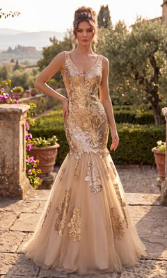 A woman in a sleeveless, champagne gold Long Sequin Mermaid Prom Dress (Chicas DR7009) stands outdoors on a stone terrace with greenery and flowers in the background.