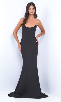 A woman with long wavy hair models the Strapless Classic Black Prom Dress: Daris by Velvi, a fitted, floor-length gown, standing against a plain white background.