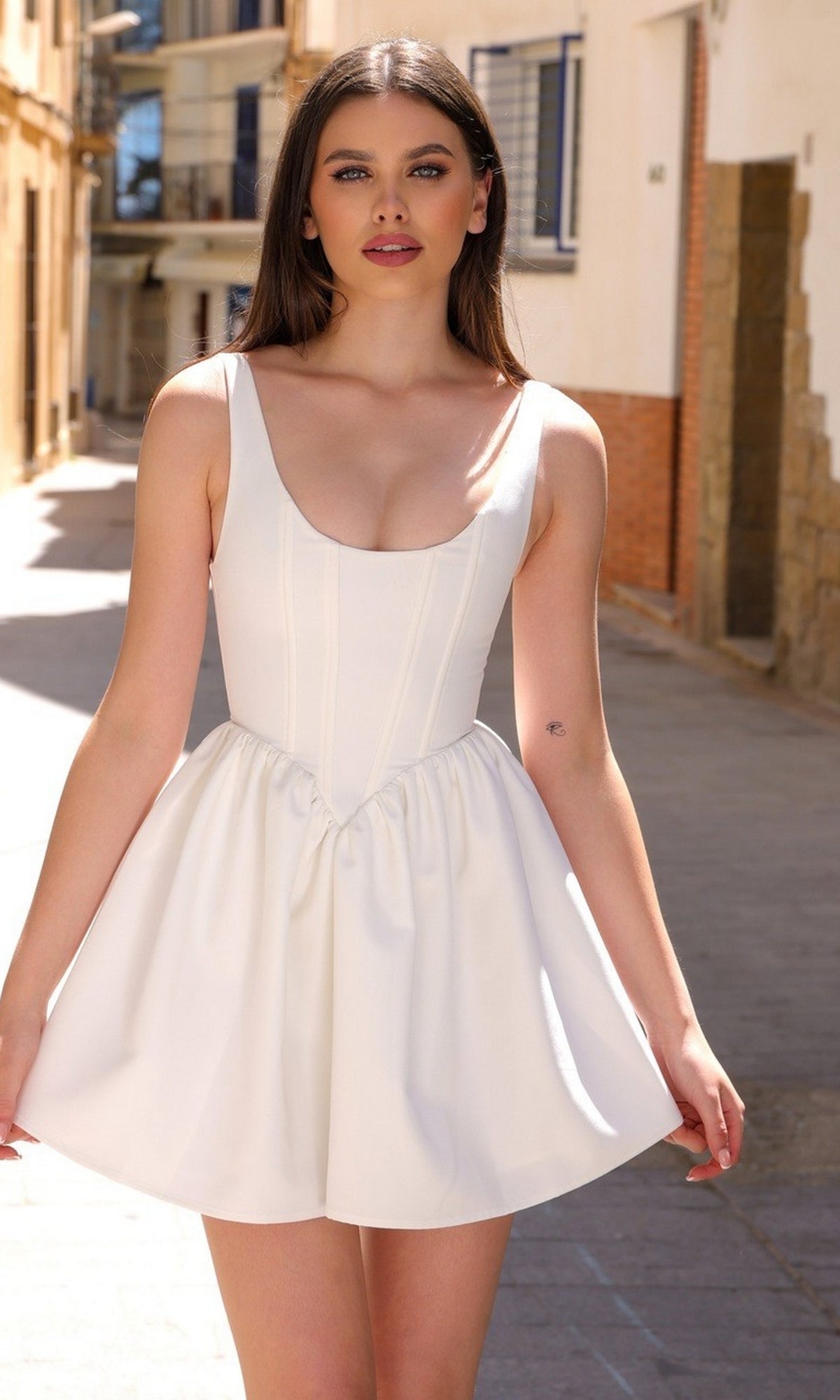 A woman with long brown hair wears the Velvi A-Line Mini Graduation Party Dress Darling, standing outdoors on a sunlit street with buildings in the background.