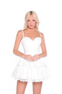Woman with long blonde hair stands against a plain white background in the Delilah—White Short Corset Graduation Dress, featuring a corset bodice and lace-trimmed tiers, perfect for graduation.