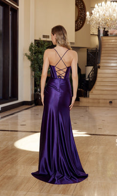 A woman stands indoors on marble flooring, wearing the Cowl-Neck Corset Pleated Satin Long Prom Dress E1042 in deep purple, featuring a cowl neck, crisscross open back, floor-length pleated satin skirt, and elegant train.