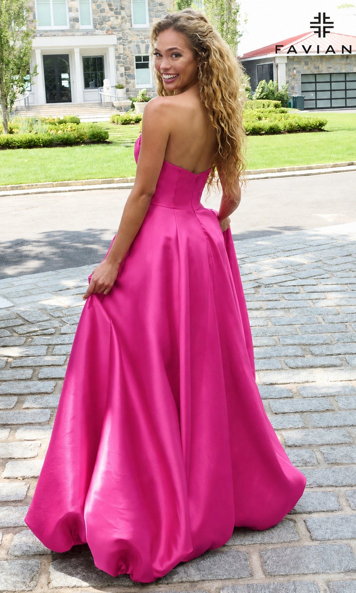 A woman wears a wild berry, strapless, A-line floor-length Faviana E11670 long prom dress while standing on a cobblestone driveway.