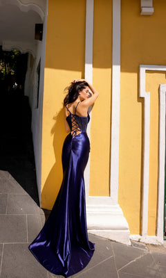 A woman stands with her back to the camera against a yellow wall, wearing the Lace-Up Corset-Bodice Long Satin Prom Dress E1292 in dark blue.